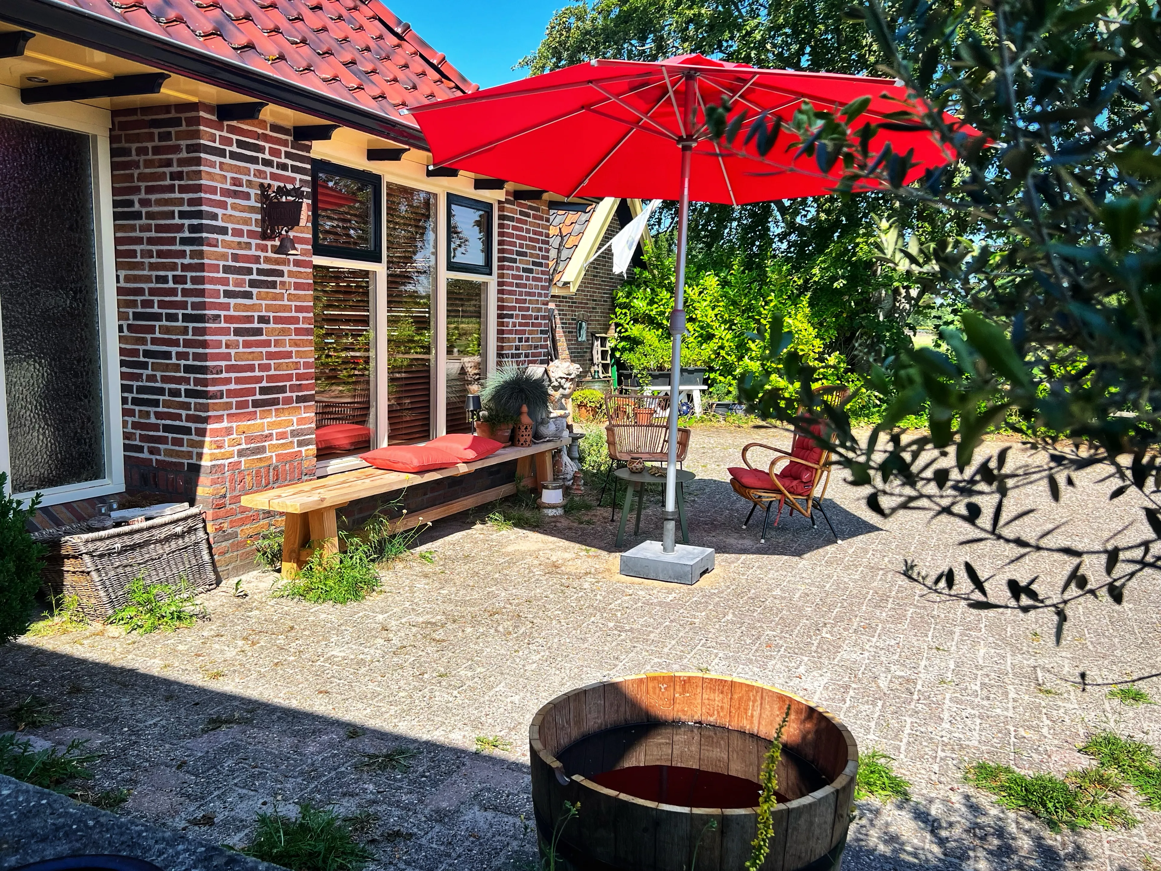 Het terras met rode parasol en zitbank tegen de karakteristieke gevel