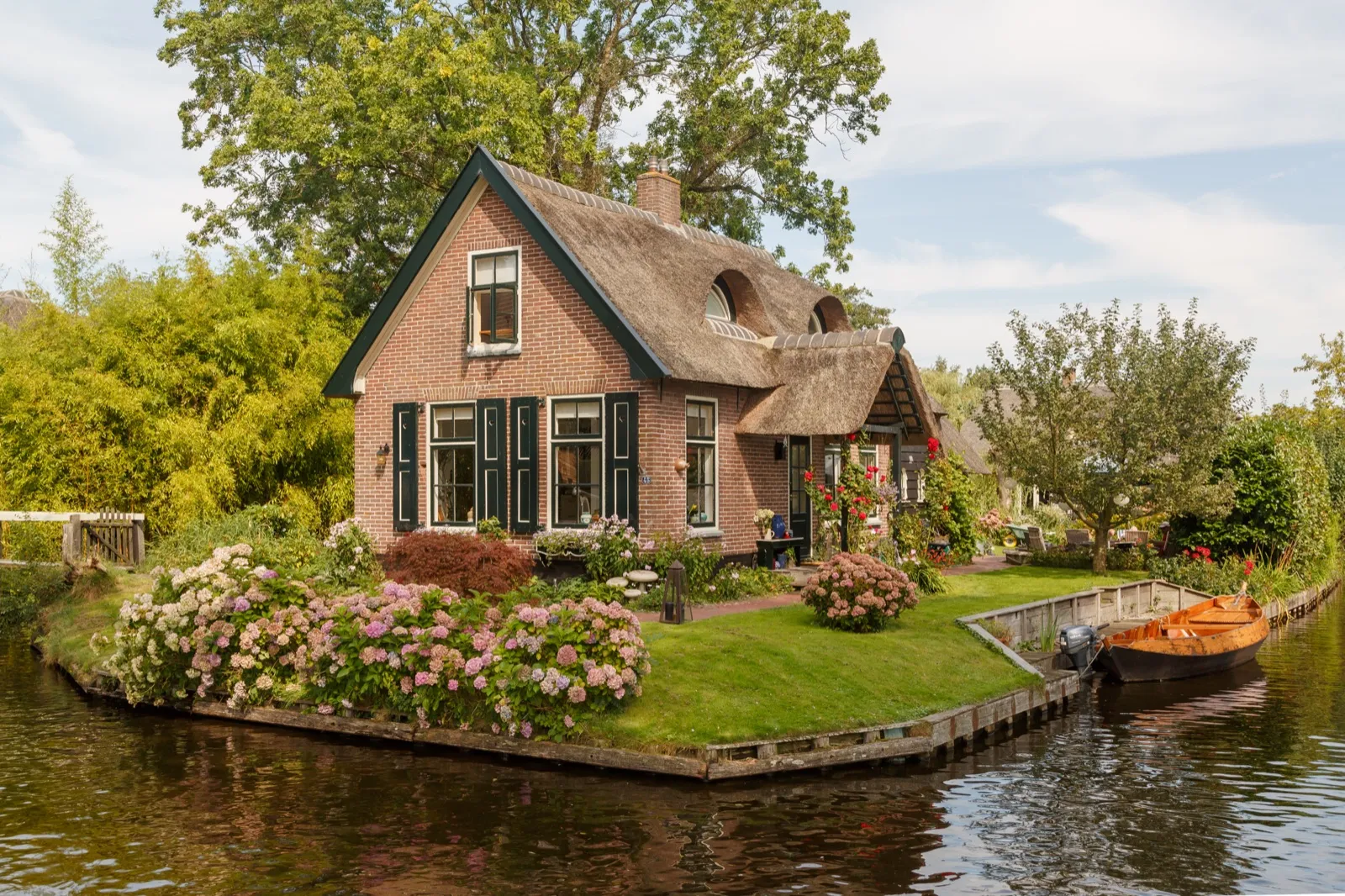 Rietgedekte boerderij aan een gracht in Giethoorn met een houten bruggetje en een bootje aan het water
