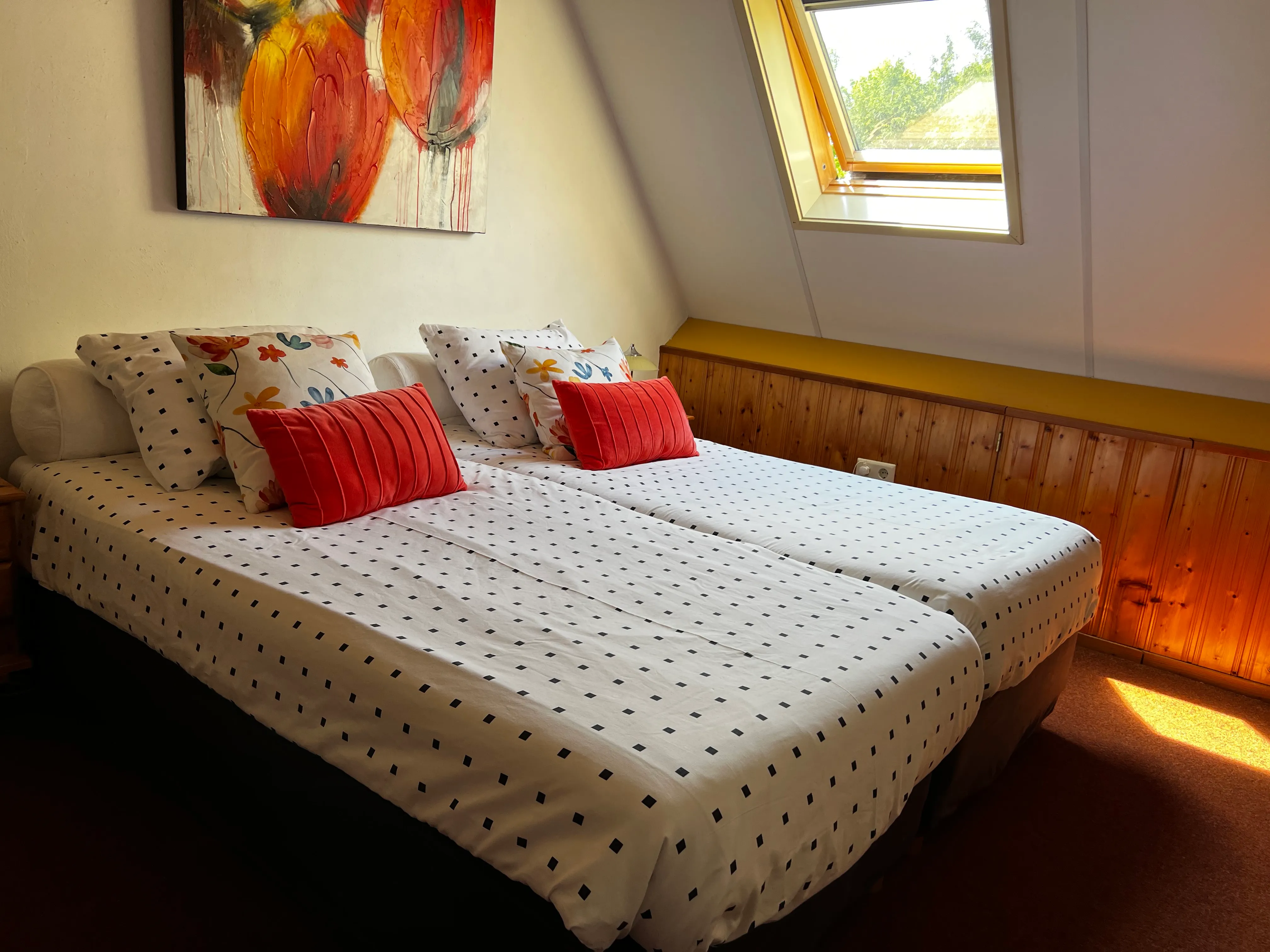 Knusse kamer met twee bedden, kussens in warme tinten en een dakraam