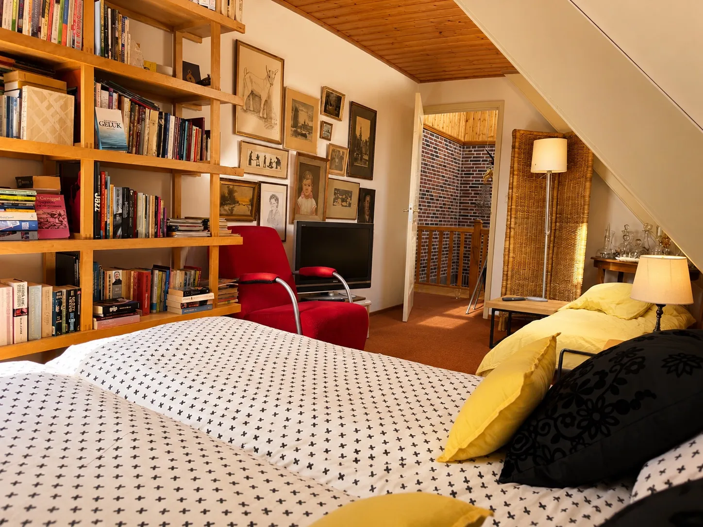 Kamer 3 De Bibliotheek met een wand vol boekenplanken, het bed en een schilderijenwand
