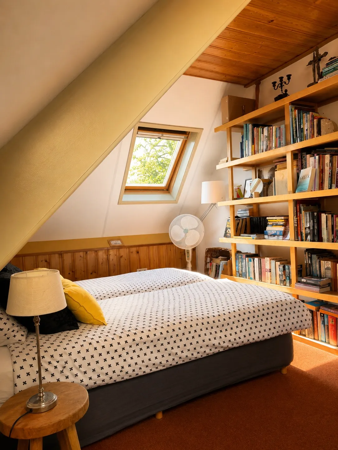 Het bed van De Bibliotheek naast een volledige boekenwand, met dakraam